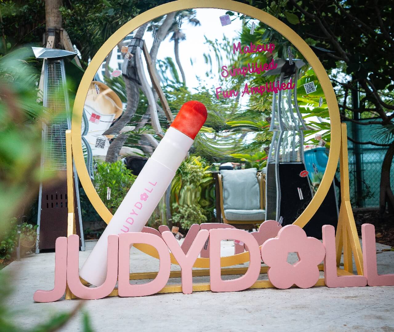 Custom Branded Mirror Photo Op Prop Fabrication Custom fabricated large circular gold mirror display featuring a giant lipstick prop, pink dimensional brand lettering, and custom typography stickers for premium outdoor corporate brand activations and event rentals.