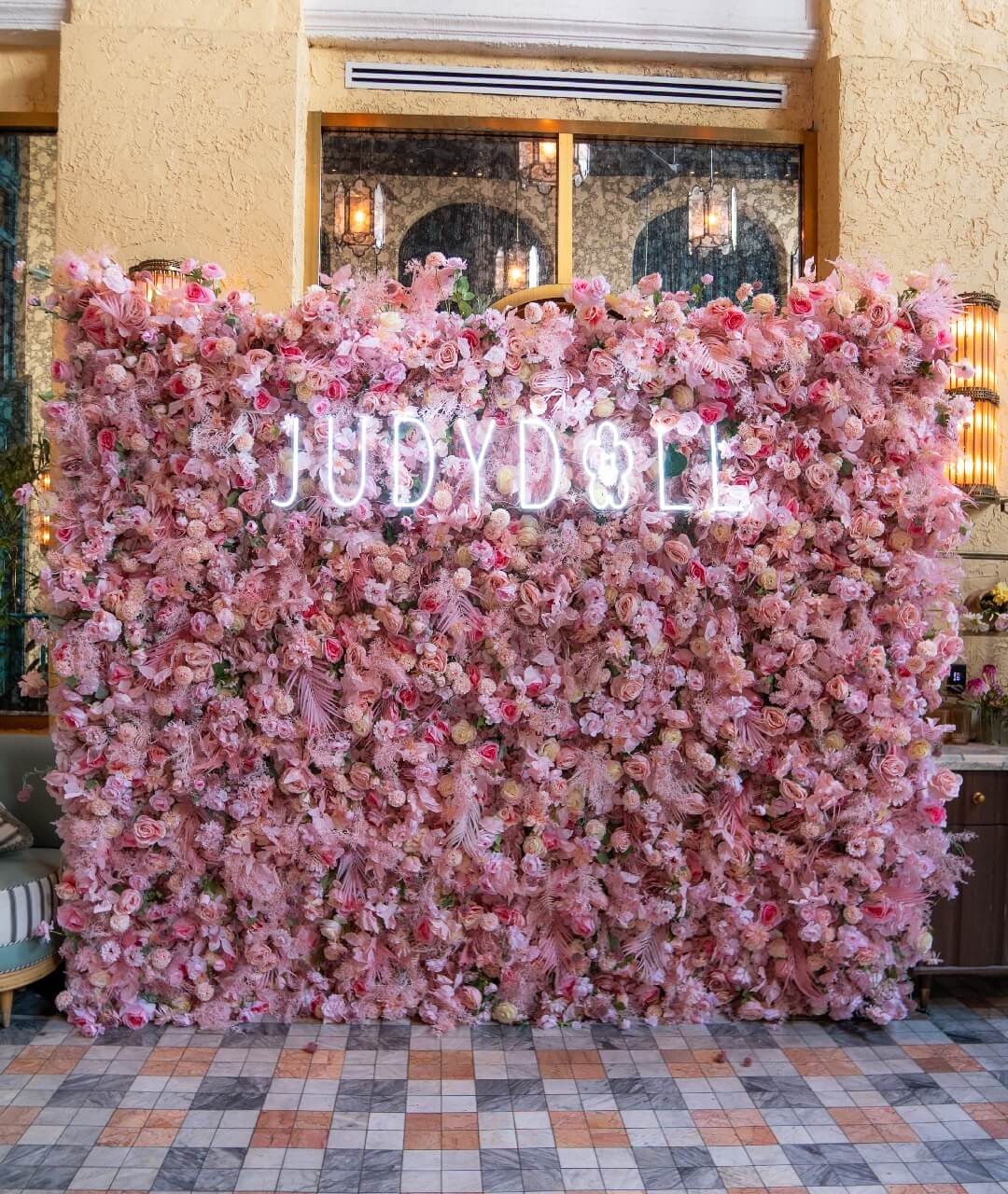 Custom Floral Wall Backdrop Brand Activation Rental Elegant corporate event backdrop featuring a massive pink floral wall integrated with a custom white neon brand sign, providing a premium photo opportunity for experiential marketing and event production rentals.